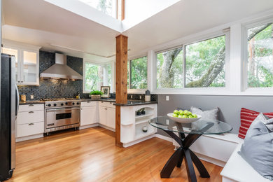 Example of a transitional eat-in kitchen design in San Francisco with flat-panel cabinets, white cabinets, black backsplash and stainless steel appliances