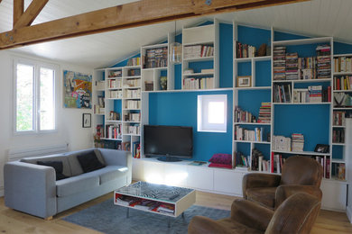 This is an example of a large open concept living room in Paris with a library, blue walls, light hardwood floors, no fireplace and a freestanding tv.