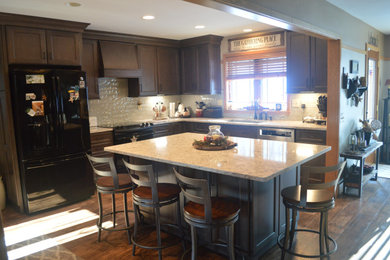 Example of an arts and crafts l-shaped kitchen design in Other with an undermount sink, shaker cabinets, distressed cabinets, quartz countertops, gray backsplash, glass tile backsplash, black appliances, an island and yellow countertops