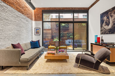 Photo of a mid-sized midcentury loft-style living room in New York with a music area, white walls, concrete floors, no fireplace, a brick fireplace surround, no tv, grey floor and brick walls.