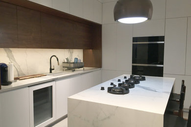 Example of a large trendy l-shaped ceramic tile and gray floor eat-in kitchen design in New York with an undermount sink, flat-panel cabinets, white cabinets, marble countertops, white backsplash, marble backsplash, paneled appliances, an island and white countertops