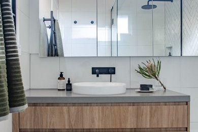 This is an example of a modern bathroom in Melbourne with flat-panel cabinets, medium wood cabinets, a drop-in tub, a corner shower, white tile, porcelain tile, white walls, porcelain floors, a vessel sink, engineered quartz benchtops, grey floor, a hinged shower door and grey benchtops.