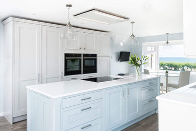 Design ideas for a medium sized galley kitchen/diner in Sussex with a submerged sink, shaker cabinets, blue cabinets, quartz worktops, stainless steel appliances, dark hardwood flooring, an island, brown floors, white worktops and feature lighting.