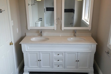 Inspiration for a mid-sized contemporary 3/4 bathroom in Toronto with recessed-panel cabinets, white cabinets, an alcove tub, a shower/bathtub combo, a two-piece toilet, black and white tile, porcelain tile, beige walls, porcelain floors, an undermount sink, solid surface benchtops, grey floor and a hinged shower door.