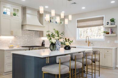 Example of a mid-sized transitional l-shaped laminate floor and beige floor kitchen pantry design in Newark with a farmhouse sink, raised-panel cabinets, gray cabinets, quartzite countertops, beige backsplash, ceramic backsplash, stainless steel appliances, an island and beige countertops