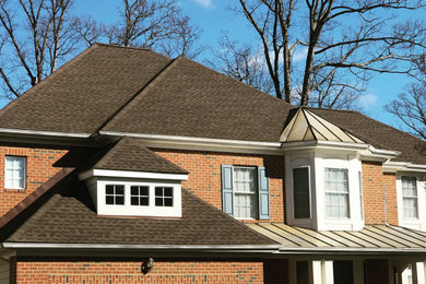Imagen de fachada de casa marrón y marrón grande de dos plantas con revestimiento de ladrillo, tejado a cuatro aguas y tejado de teja de madera