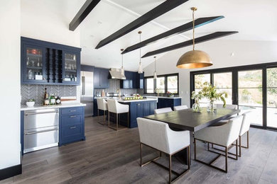 Expansive contemporary u-shaped open plan kitchen in Los Angeles with a farmhouse sink, shaker cabinets, blue cabinets, quartz benchtops, glass tile splashback, stainless steel appliances, medium hardwood floors, with island, grey floor and white benchtop.