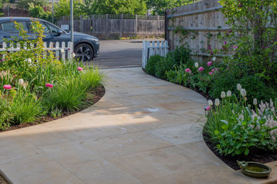 This is an example of a small contemporary front partial sun garden in London with a garden path, natural stone paving and a wood fence.