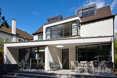 This is an example of a mid-sized contemporary two-storey stucco white house exterior in London with a tile roof.