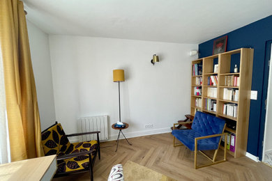Cette image montre un petit salon bohème avec une bibliothèque ou un coin lecture, un mur bleu, parquet clair et un sol marron.