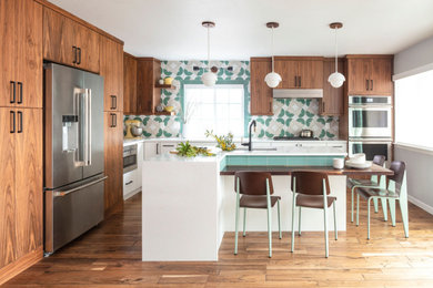 Example of a mid-sized 1950s l-shaped medium tone wood floor, brown floor and tray ceiling open concept kitchen design in Denver with an undermount sink, flat-panel cabinets, medium tone wood cabinets, quartz countertops, multicolored backsplash, ceramic backsplash, stainless steel appliances, an island and white countertops