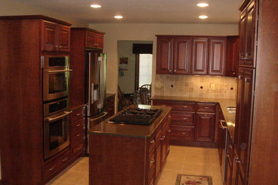 Photo of a mid-sized traditional l-shaped eat-in kitchen in Detroit with an undermount sink, raised-panel cabinets, red cabinets, beige splashback, ceramic splashback, stainless steel appliances, ceramic floors and with island.