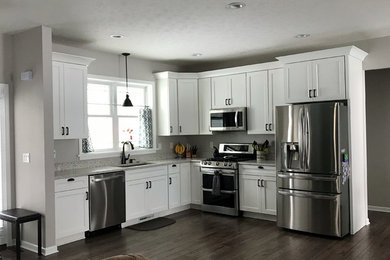Inspiration for a mid-sized contemporary l-shaped dark wood floor and brown floor open concept kitchen remodel in New York with an undermount sink, shaker cabinets, white cabinets, terrazzo countertops, stainless steel appliances, an island and white countertops