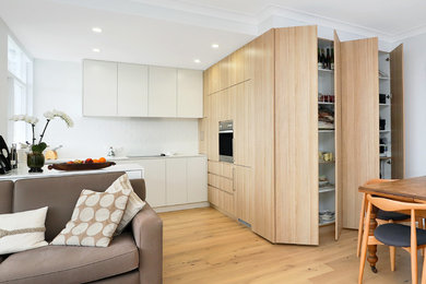 Inspiration for a mid-sized scandinavian u-shaped open plan kitchen in Sydney with an undermount sink, flat-panel cabinets, white cabinets, quartz benchtops, white splashback, subway tile splashback, stainless steel appliances, light hardwood floors, a peninsula, yellow floor and white benchtop.