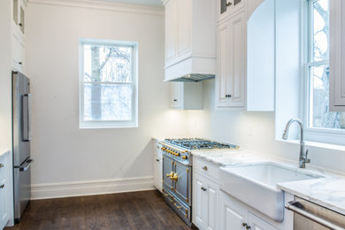Example of a mid-sized cottage galley dark wood floor and brown floor kitchen design in New York with a drop-in sink, raised-panel cabinets, white cabinets, marble countertops, white backsplash, stainless steel appliances and white countertops