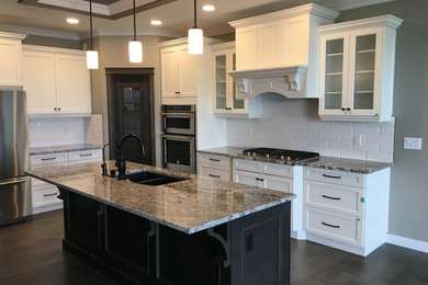 This is an example of a mid-sized transitional l-shaped kitchen in Edmonton with a double-bowl sink, shaker cabinets, white cabinets, granite benchtops, white splashback, subway tile splashback, stainless steel appliances, medium hardwood floors, with island and brown floor.