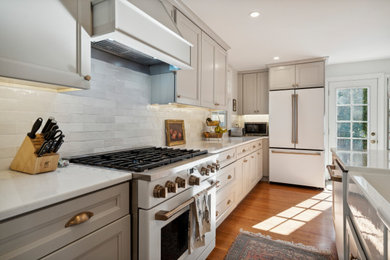 Eat-in kitchen - mid-sized galley light wood floor and brown floor eat-in kitchen idea in Philadelphia with a drop-in sink, flat-panel cabinets, white cabinets, quartz countertops, white backsplash, ceramic backsplash, stainless steel appliances, an island and white countertops