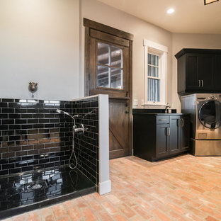 Large rustic l-shaped utility room in Denver with black cabinets, composite countertops, grey walls, brick flooring, a side by side washer and dryer, red floors and shaker cabinets.