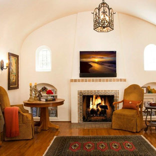 Ejemplo de salón para visitas cerrado, mediterráneo, grande, con paredes beige, suelo de madera en tonos medios, chimenea tradicional, marco de chimenea de baldosas y/o azulejos y televisor colgado en la pared