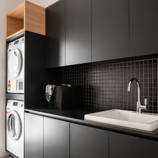 パースのコンテンポラリースタイルのおしゃれな家事室 (ドロップインシンク、フラットパネル扉のキャビネット、黒いキャビネット、上下配置の洗濯機・乾燥機、黒いキッチンカウンター) の写真
