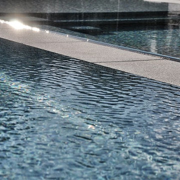 glass tile swimming pool + spa with perimeter overflow + granite decking