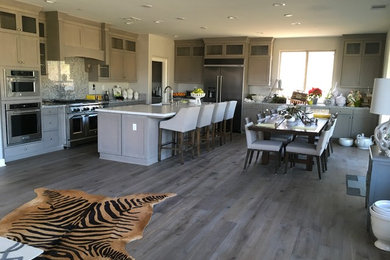 This is an example of a mid-sized contemporary l-shaped open plan kitchen in Orange County with a farmhouse sink, shaker cabinets, stone slab splashback, stainless steel appliances, medium hardwood floors, with island, grey floor, white benchtop, grey cabinets, quartz benchtops and grey splashback.