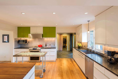Kitchen - scandinavian u-shaped medium tone wood floor kitchen idea in Minneapolis with an undermount sink, flat-panel cabinets, white cabinets, marble countertops, white backsplash, stainless steel appliances and black countertops