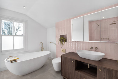 Design ideas for a large contemporary bathroom in London with flat-panel cabinets, dark wood cabinets, a freestanding bath, a wall mounted toilet, pink tiles, ceramic tiles, white walls, ceramic flooring, wooden worktops, beige floors, an open shower, brown worktops, a chimney breast, a single sink, a freestanding vanity unit and a vaulted ceiling.