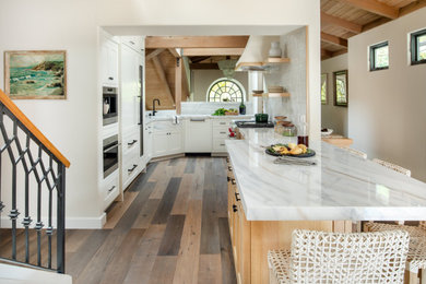 Example of a small beach style l-shaped medium tone wood floor and brown floor kitchen design in Orange County with shaker cabinets, white cabinets, an island, an undermount sink, stainless steel appliances and white countertops