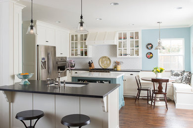 Elegant medium tone wood floor eat-in kitchen photo in Dallas with an undermount sink, glass-front cabinets, white cabinets, white backsplash, subway tile backsplash, stainless steel appliances and an island