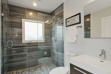 This is an example of a mid-sized contemporary bathroom in San Francisco with flat-panel cabinets, brown cabinets, a curbless shower, a one-piece toilet, gray tile, grey walls and an integrated sink.