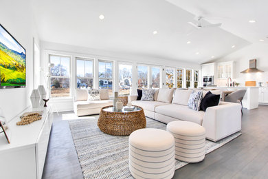 Example of a mid-sized beach style open concept medium tone wood floor and vaulted ceiling family room design in New York with white walls, no fireplace and a wall-mounted tv
