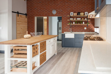 Example of a large cottage l-shaped vinyl floor, gray floor and exposed beam kitchen design in Other with a farmhouse sink, shaker cabinets, blue cabinets, marble countertops, beige backsplash, marble backsplash, white appliances, an island and white countertops
