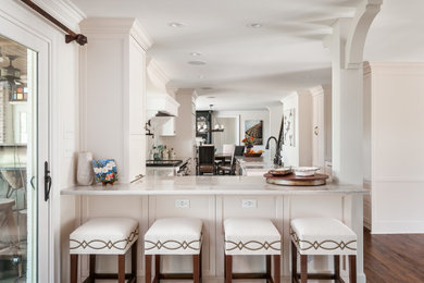 Mid-sized elegant medium tone wood floor and brown floor kitchen photo in Other with a farmhouse sink, shaker cabinets, white cabinets, quartzite countertops, white backsplash, mosaic tile backsplash, stainless steel appliances, an island and white countertops