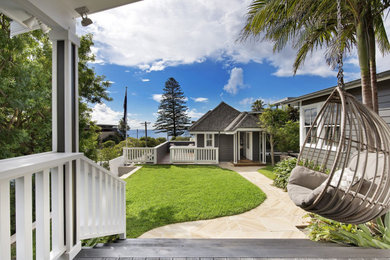 This is an example of a mid-sized beach style backyard verandah in Sydney with decking, an awning and wood railing.