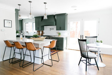 Mid-sized transitional galley eat-in kitchen in Denver with a farmhouse sink, shaker cabinets, green cabinets, quartz benchtops, white splashback, brick splashback, stainless steel appliances, medium hardwood floors, a peninsula, brown floor and white benchtop.