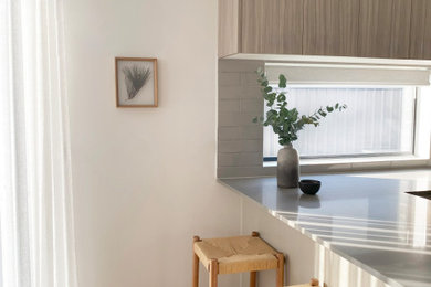 Inspiration for a small contemporary u-shaped kitchen in Melbourne with a double-bowl sink, beige cabinets, quartz benchtops, beige splashback, porcelain splashback, black appliances, laminate floors, with island, brown floor and grey benchtop.