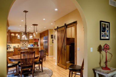 Large elegant u-shaped light wood floor and brown floor eat-in kitchen photo in Minneapolis with raised-panel cabinets, medium tone wood cabinets, beige backsplash, stone tile backsplash, stainless steel appliances, an island, a farmhouse sink, multicolored countertops and quartz countertops