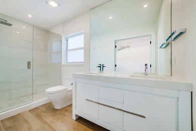 Alcove shower - mid-sized modern master gray tile and porcelain tile porcelain tile, brown floor and double-sink alcove shower idea in Miami with flat-panel cabinets, white cabinets, a one-piece toilet, white walls, an undermount sink, quartz countertops, a hinged shower door, white countertops, a niche and a freestanding vanity