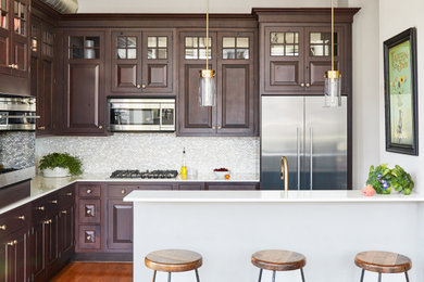 Small trendy l-shaped medium tone wood floor and brown floor open concept kitchen photo in Chicago with raised-panel cabinets, dark wood cabinets, quartzite countertops, white backsplash, ceramic backsplash, stainless steel appliances, an island and white countertops