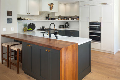 Example of a small classic l-shaped eat-in kitchen design in San Diego with recessed-panel cabinets, wood countertops, white backsplash, stainless steel appliances, a peninsula and brown countertops