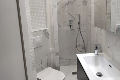 Cette photo montre une petite salle d'eau moderne avec des portes de placard noires, une douche à l'italienne, WC suspendus, un carrelage blanc, des carreaux de céramique, un mur blanc, un sol en carrelage de céramique, un lavabo intégré, un plan de toilette en surface solide, un sol gris et un plan de toilette blanc.