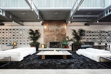 Photo of an expansive industrial open plan living room in London with white walls, concrete flooring, a standard fireplace, a metal fireplace surround, a freestanding tv and grey floors.