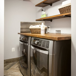 This is an example of a small rustic l-shaped utility room in DC Metro with wood worktops, grey walls, porcelain flooring, a side by side washer and dryer and brown floors.