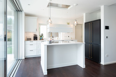 Kleine Landhausstil Küche mit weißen Schränken, Rückwand-Fenster, schwarzen Elektrogeräten, dunklem Holzboden, Kücheninsel, braunem Boden und weißer Arbeitsplatte in München
