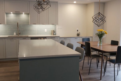 Foto på ett mellanstort funkis grå kök, med en undermonterad diskho, skåp i shakerstil, blå skåp, bänkskiva i kvarts, blått stänkskydd, stänkskydd i glaskakel, rostfria vitvaror, vinylgolv, en köksö och brunt golv