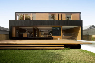 Photo of a large modern two-storey black house exterior in Sydney with wood siding, a flat roof and a metal roof.