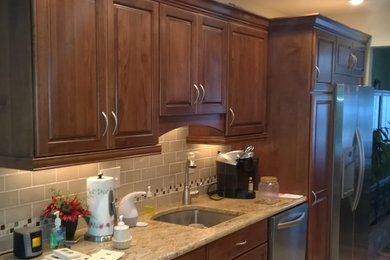 Inspiration for a mid-sized timeless galley porcelain tile eat-in kitchen remodel in New York with an undermount sink, raised-panel cabinets, brown cabinets, granite countertops, beige backsplash, glass tile backsplash and stainless steel appliances