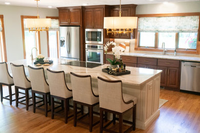 Example of a mid-sized classic l-shaped medium tone wood floor and brown floor eat-in kitchen design in Other with an undermount sink, raised-panel cabinets, brown cabinets, quartzite countertops, white backsplash, ceramic backsplash, stainless steel appliances, an island and white countertops