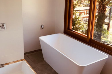 This is an example of a mid-sized modern master bathroom in Sydney with light wood cabinets, a freestanding tub, an open shower, white tile, ceramic tile, white walls, ceramic floors and grey floor.